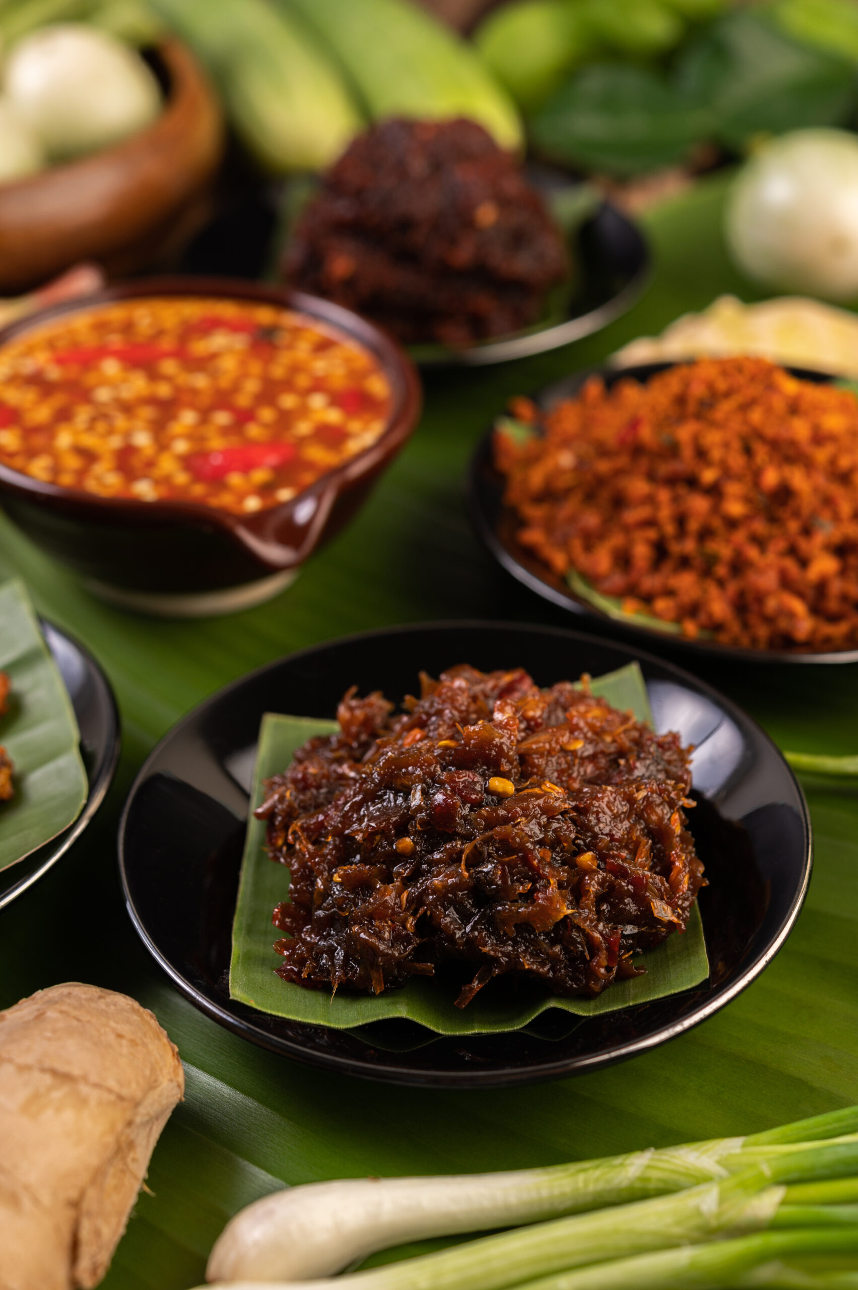 Chili paste is served on banana leaves on a plate with long beans, lime, chili, and eggplant.
